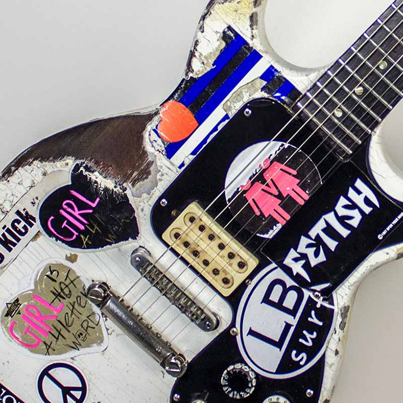 Zoom of Joan Jett's guitar with various stickers such as "Girls Kick", "Fetish", and "Distortion."